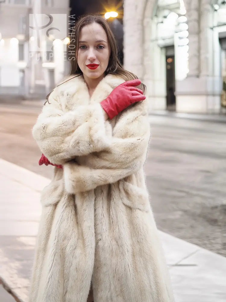 Beige mink fur coat close-up with open neckline and textured fur, held by red gloves