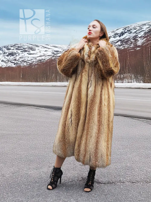 Long hooded fur coat in tan and brown with open front, standing collar and long sleeves.