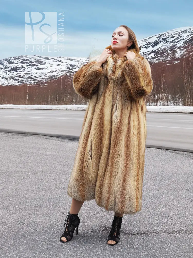 Long hooded fur coat in tan and brown with open front, standing collar and long sleeves.
