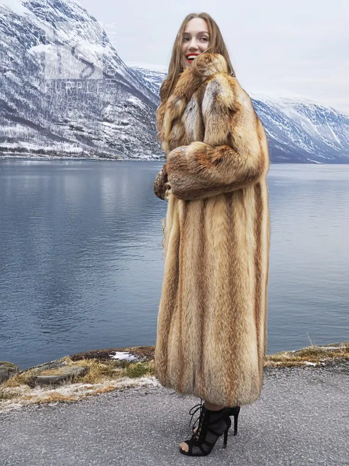 Long tan fur coat with open front; model facing camera, arms crossed over chest.