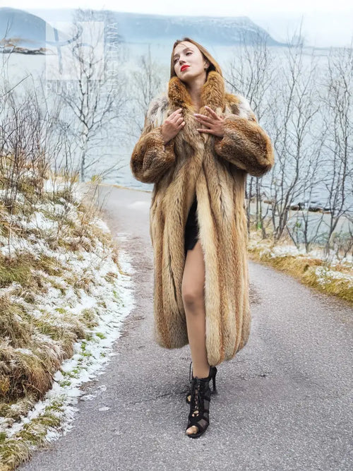 Long fur coat with open front, tan color, full sleeves; model holding lapels close.