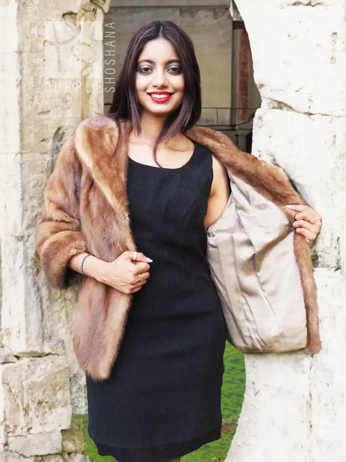 Beige mink fur opera jacket worn over black dress, shawl collar and short sleeves.