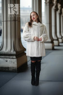 A woman wearing a fluffy white faux fur coat, black mini skirt, and black over-the-knee boots stands in a colonnade with large stone columns.