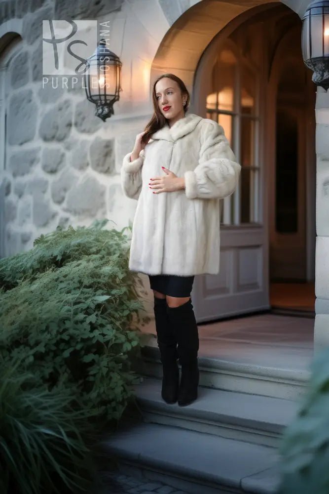 A woman stands on the steps of a stone building wearing a voluminous cream faux-fur coat, a black mini skirt, and black knee-high boots.